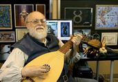 Photograph of a balding man with a gray beard playing a lute