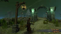 Screenshot of a medieval figure on a dimly-lit path approaching a stone archway. A tall lantern appears over him.